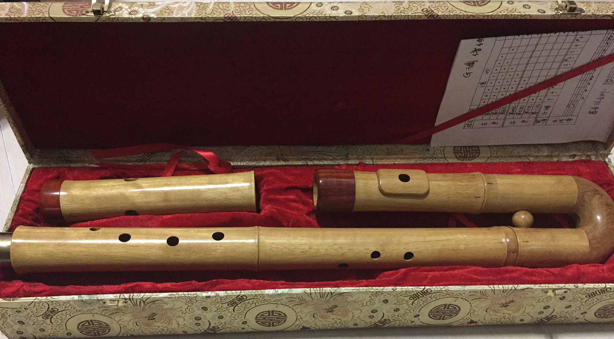 The various pieces of a lower-ranged Chinese bamboo flute, including its curved mouthpiece joint, in a flute case. 