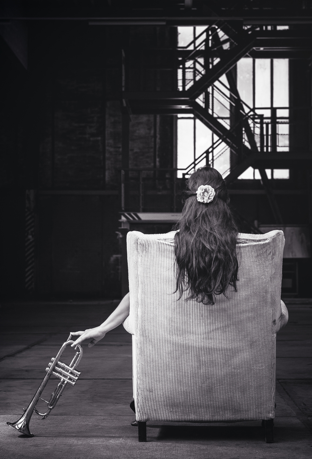 The back of a chair showing the long hair of a woman sitting in it and holding a trumpet. Photo by Alex via Unsplash *(https://unsplash.com/@worthyofelegance)