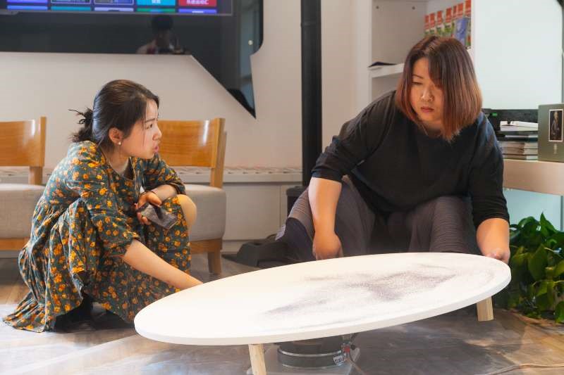 Xia Yuyan talking with Luan Jiaqi in front of a circular table.