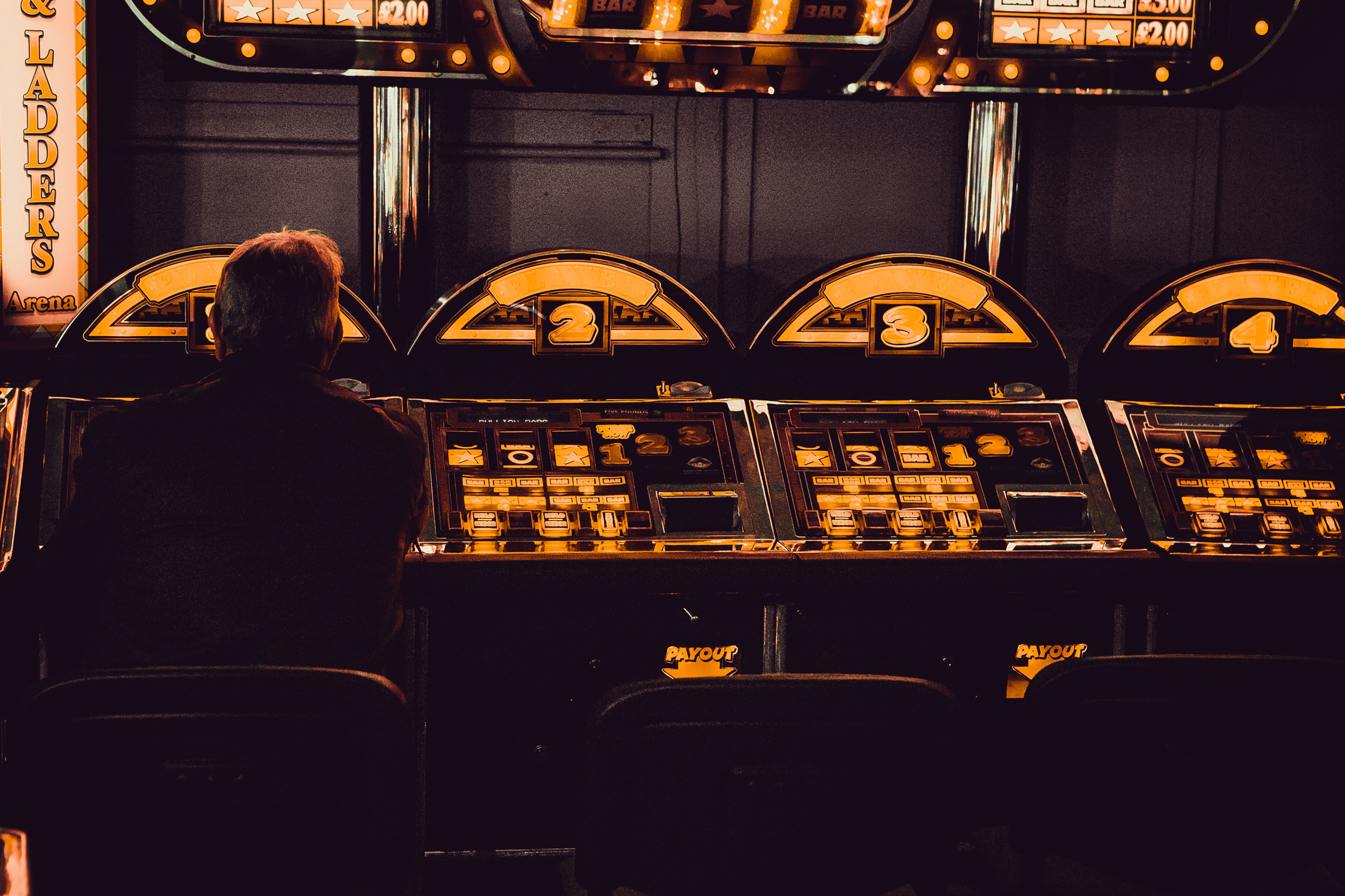 A lone gambler playing one of a group of slot machines (Photo by Carl Raw on Unsplash)