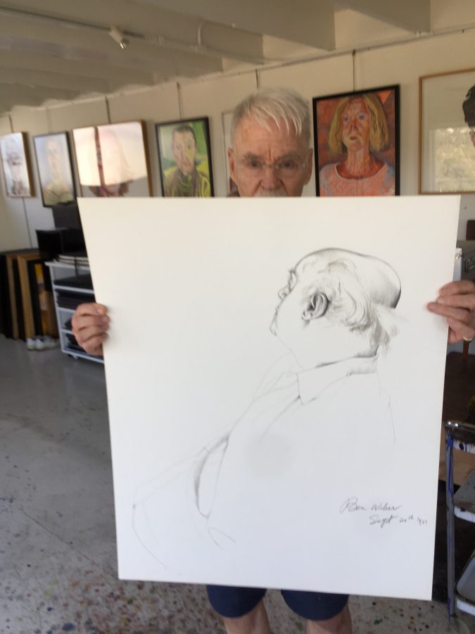Don Bachardy in his studio holding up one of his portraits of Ben Weber.