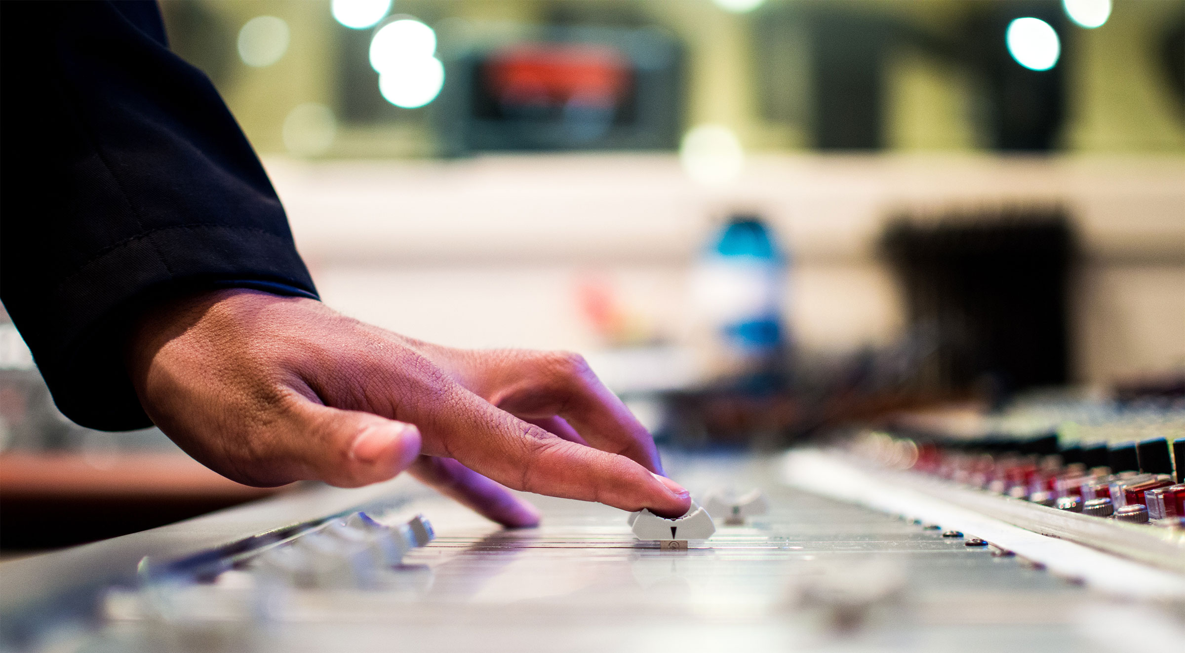 A photo of a person at a mixing desk using their finger to slide one of the controls