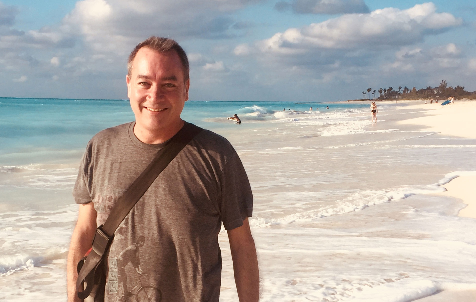 A man in a grey t shirt posing on the beach