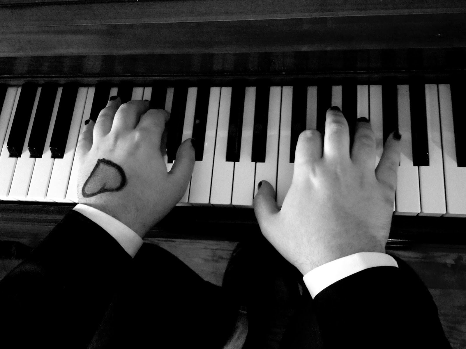 Hands on a piano, with a heart tattoo on the left hand.