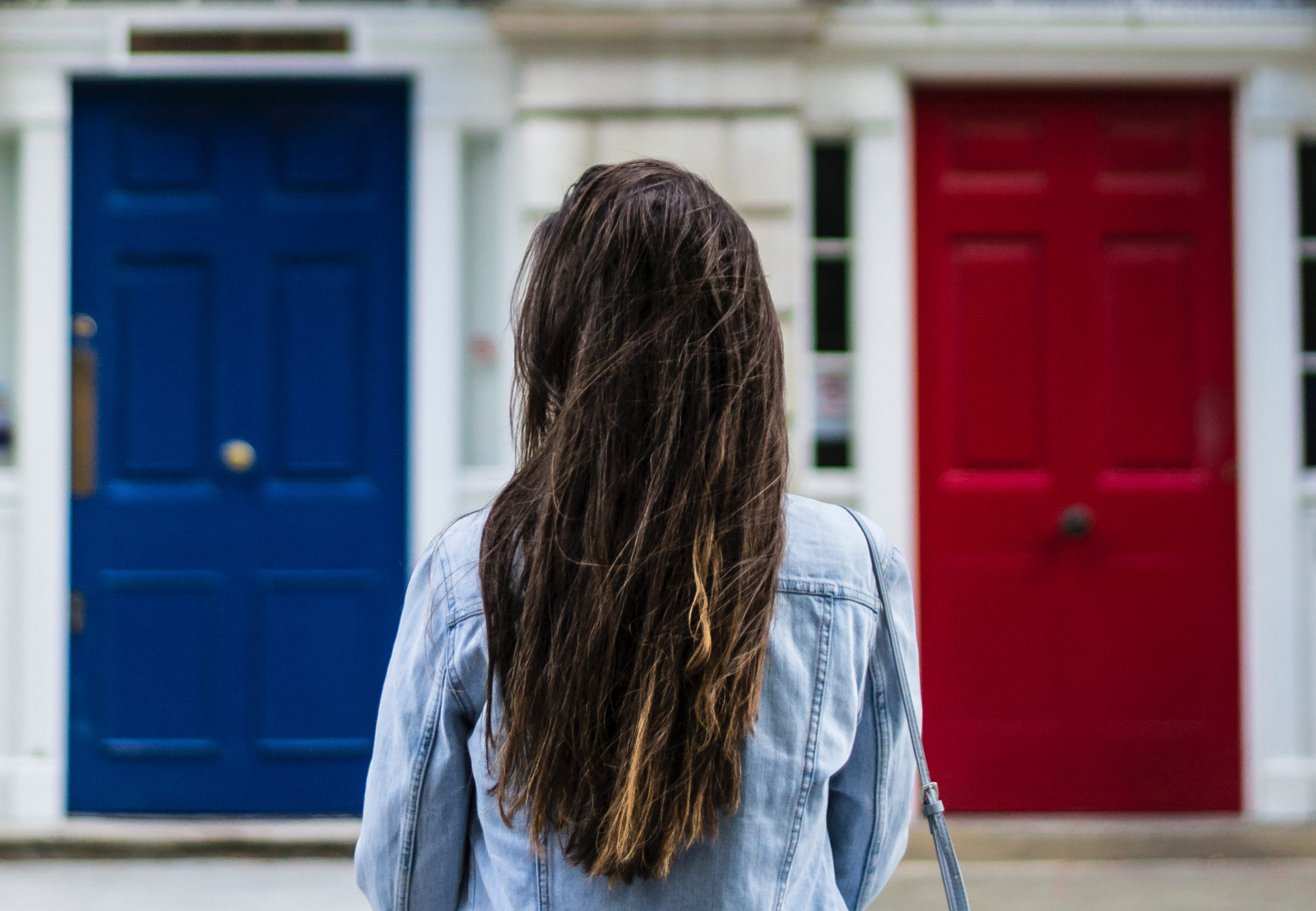 A woman with her back facing the camera standing between a blue door and a red door