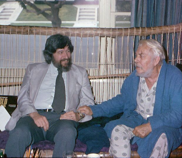 Ben Johnston, wearing a jacket and tie, sitting outside with Harry Partch in 1974