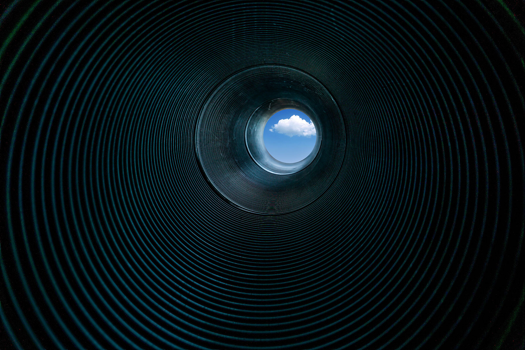 A tunnel with a blue sky peeking out of the end