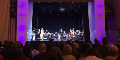 Members of the Afro Yaqui Music Collective performing on a proscenium stage in front of a large audience.