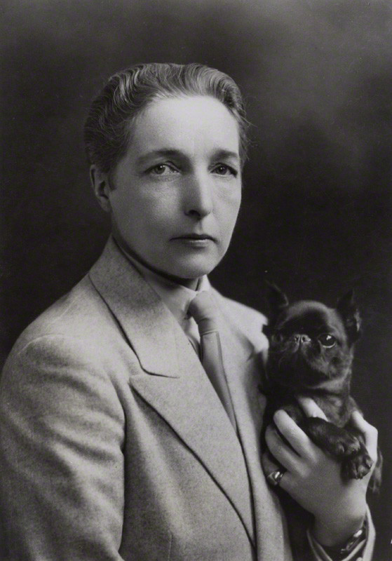 Radclyffe Hall in a jacket and tie holding a dog.