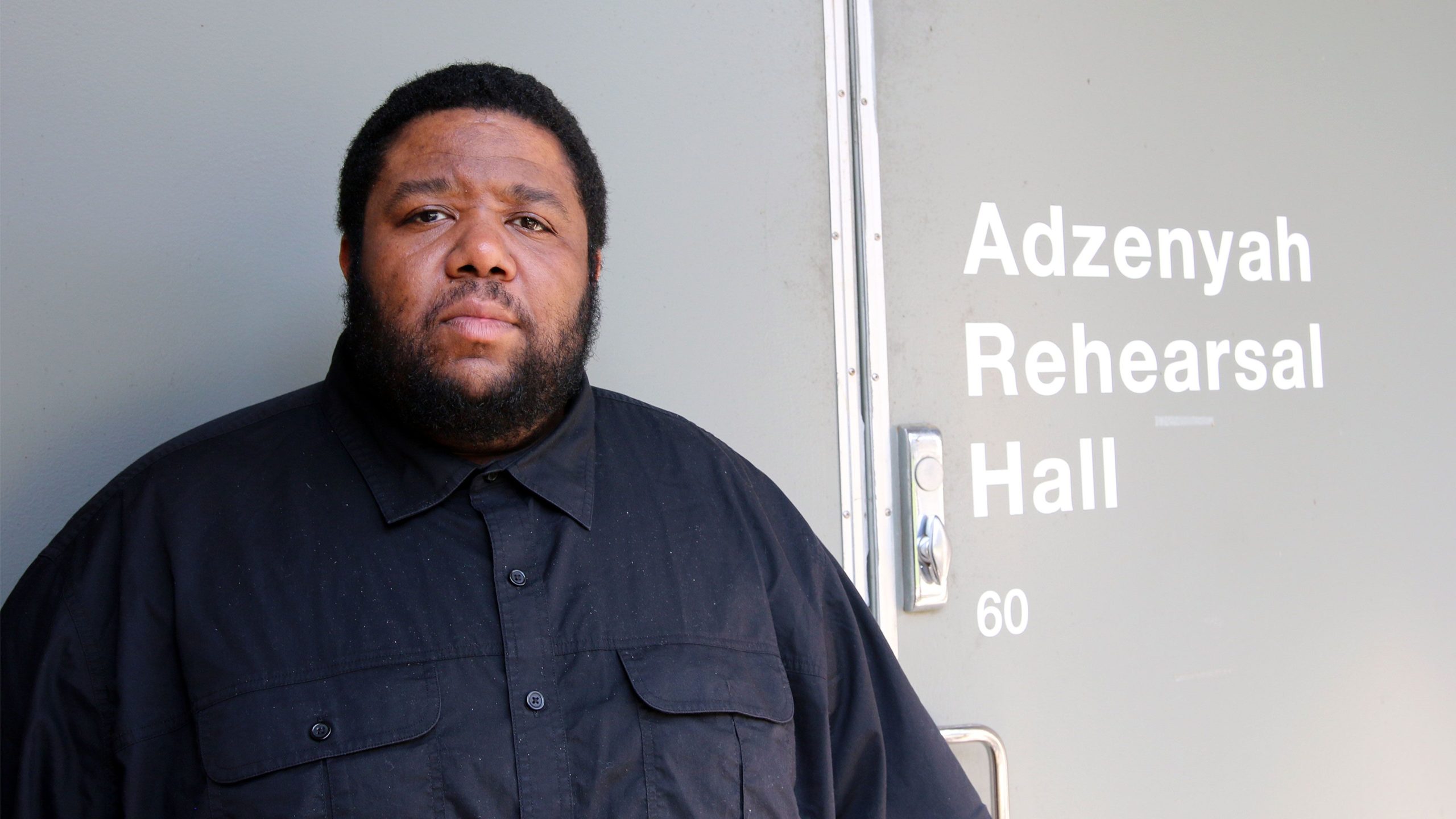 A BIPOC man posing in front of a rehearsal hall door
