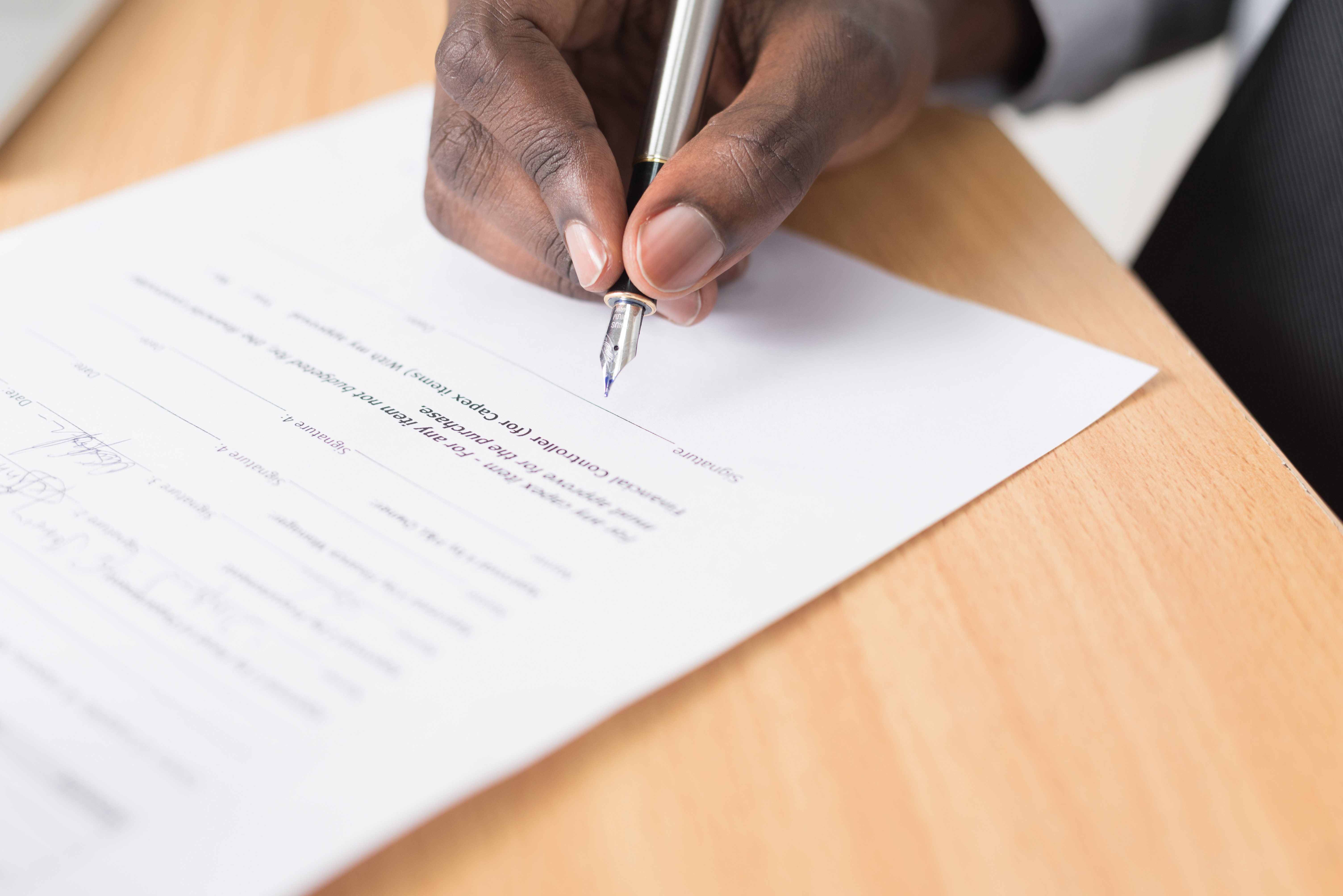 An unidentified hand signing a paper contract on a table.