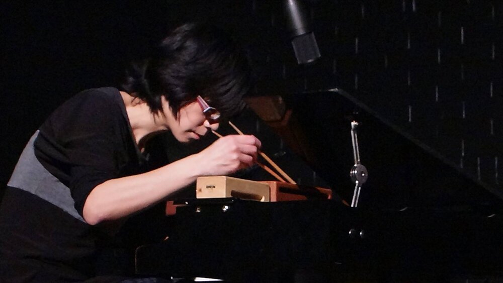 A performer at a toy piano with chopsticks