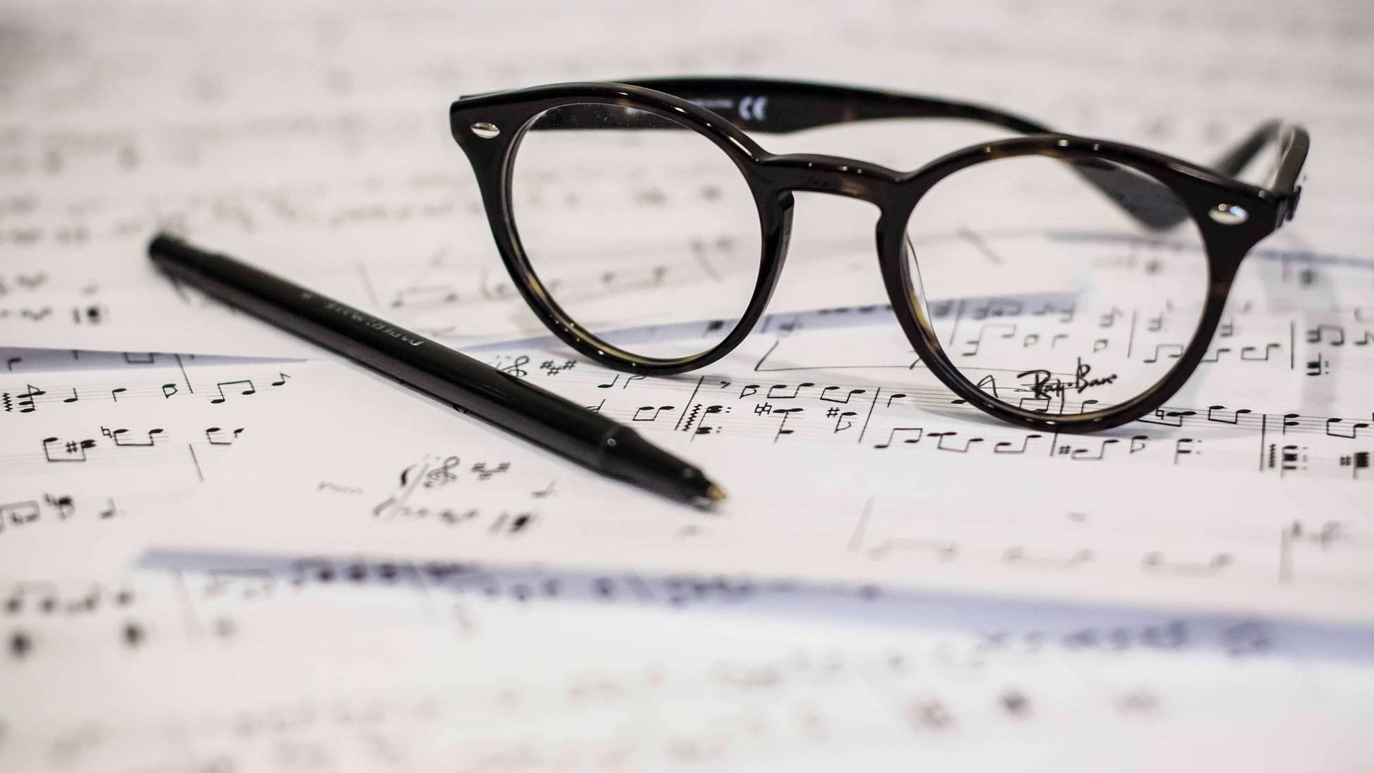 A pair of eyeglasses and a pen on top of pages of music notation.