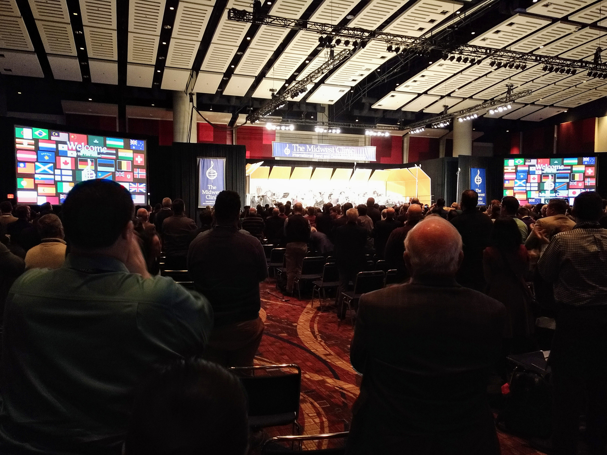 The audience applauding at the conclusion of a wind band concert at the 2019 Midwest Clinic at McCormick Place in Chicago. Signage includes a composite image of flags from all over the world reflecting the nationalities of this year';s performing ensembles. 
