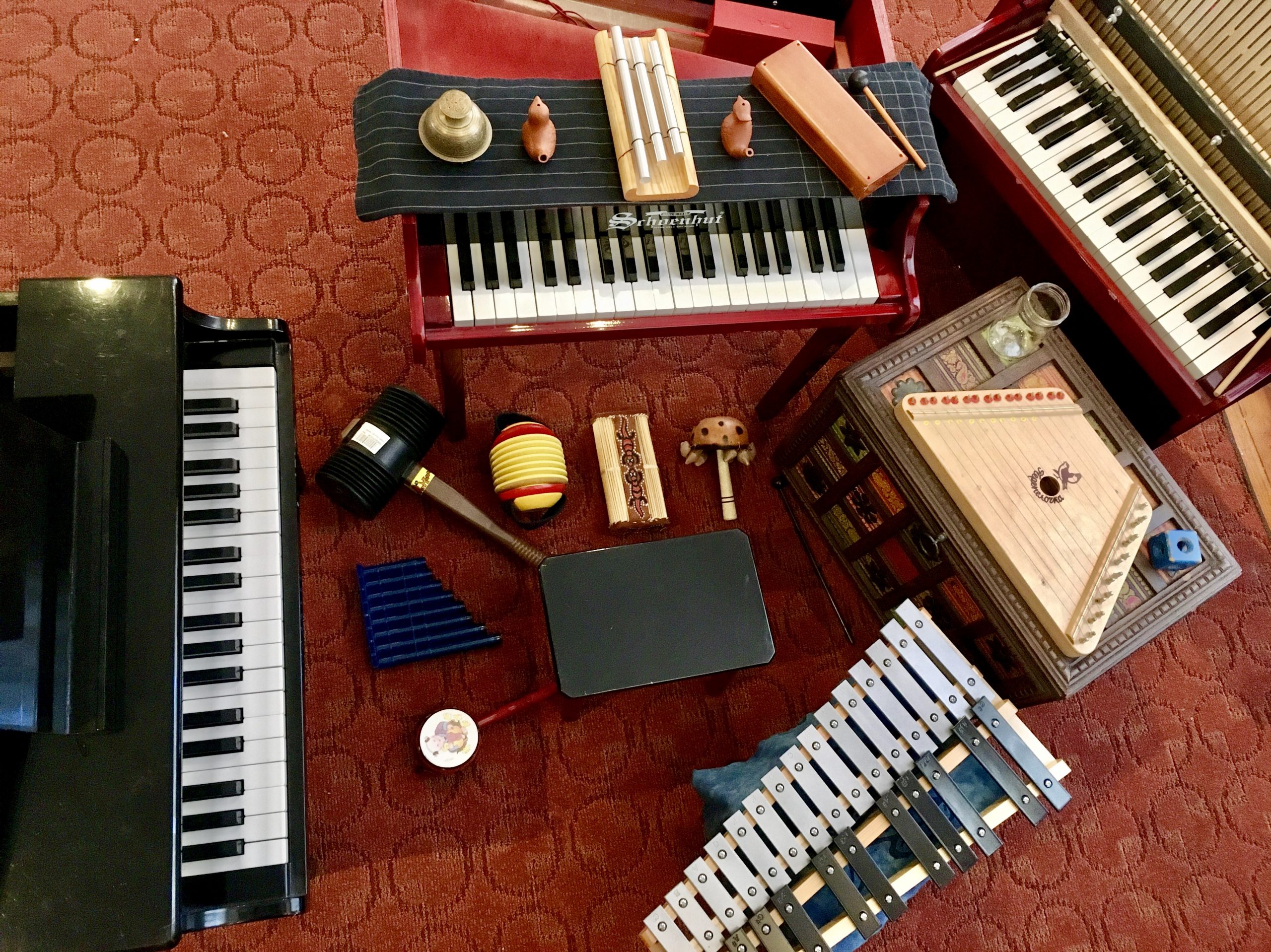 An array of toy keyboards, a toy zither, and a toy mallet instrument in a circle on the floor.