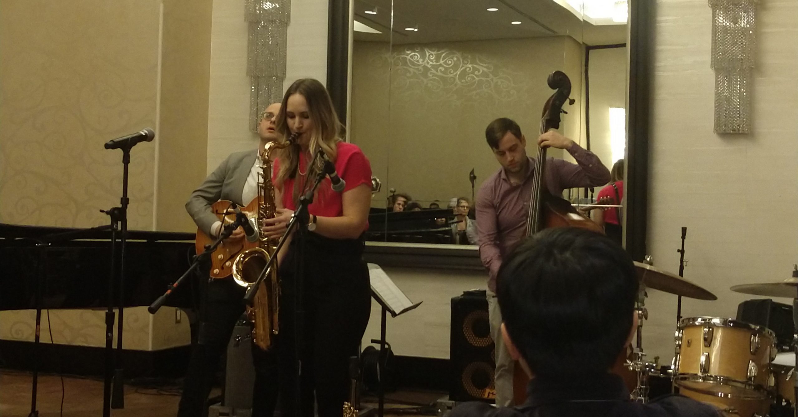 Roxy Coss performing on saxophone with members of her Quintet.