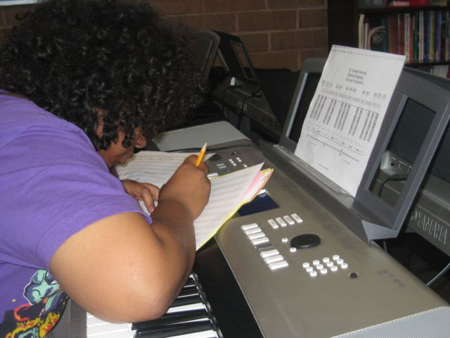 A student composer working on a score in front of an electronic keyboard.