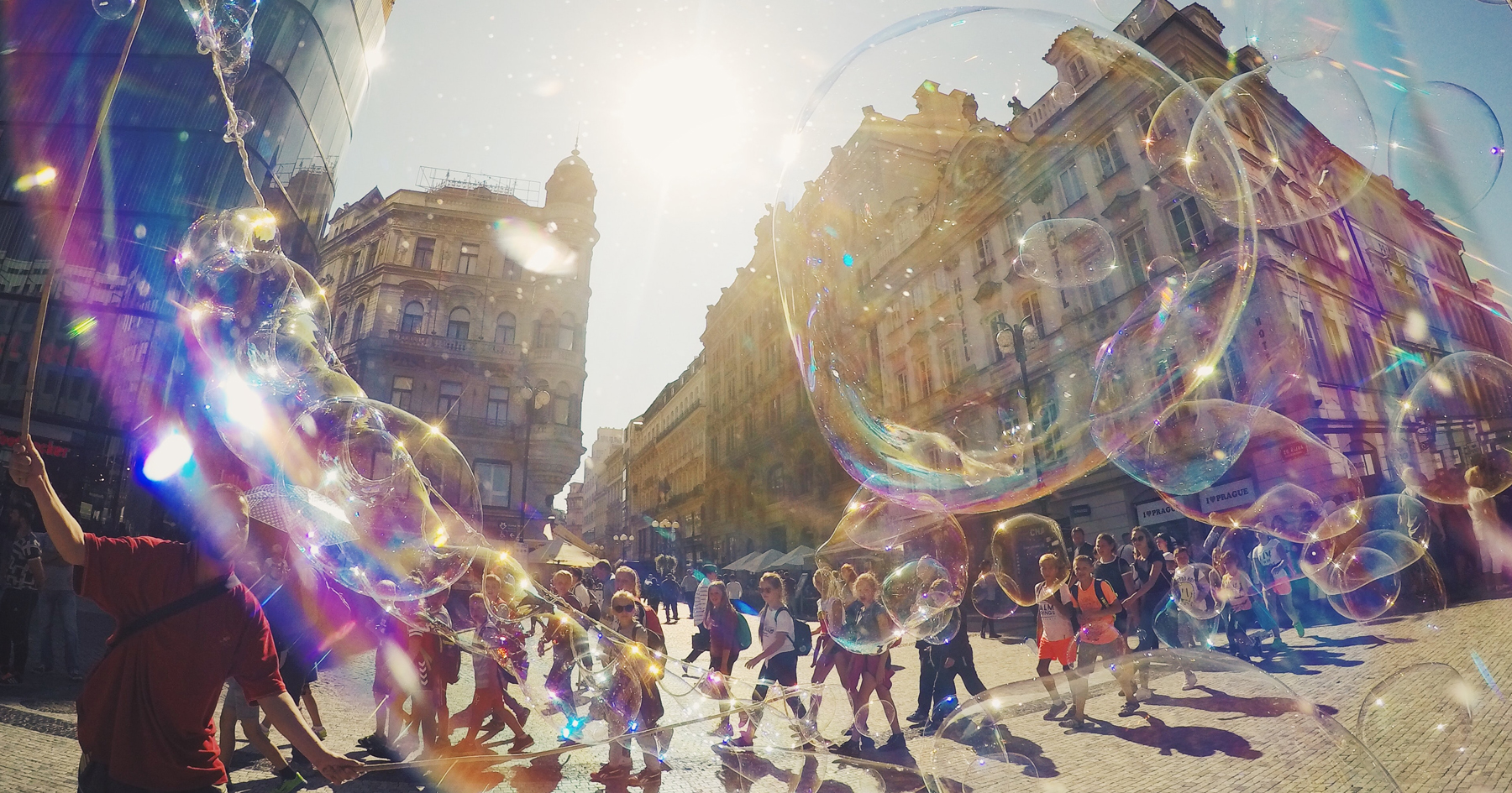 Children blowing large bubbles in a public square in Prague.