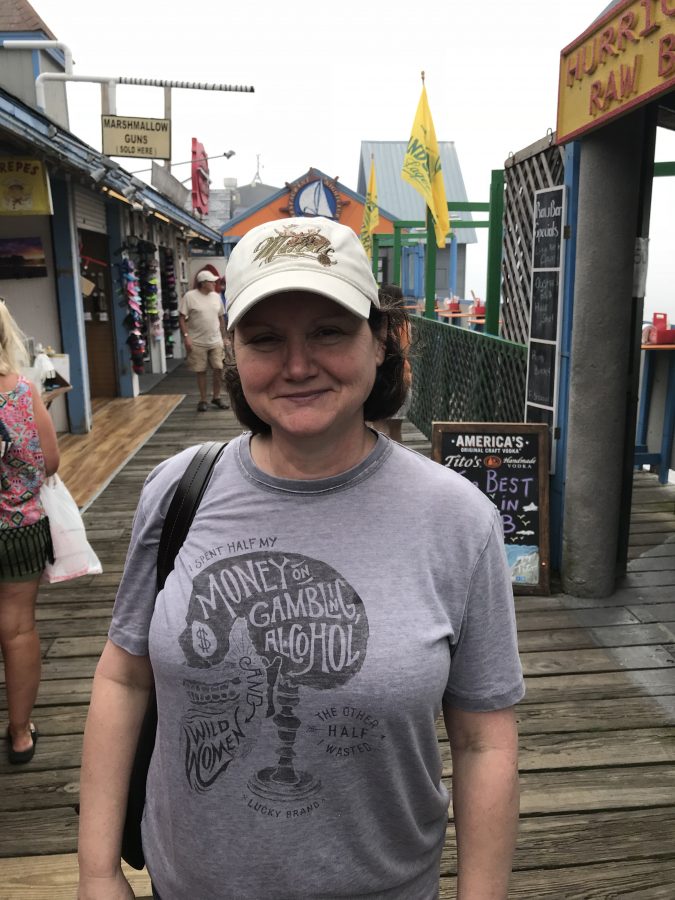Julie Giroux walking on a boardwalk wearing a cap and a T-shirt which reads: "I spent half my money on gambling, alcohol, and wild women; the other half wasted."