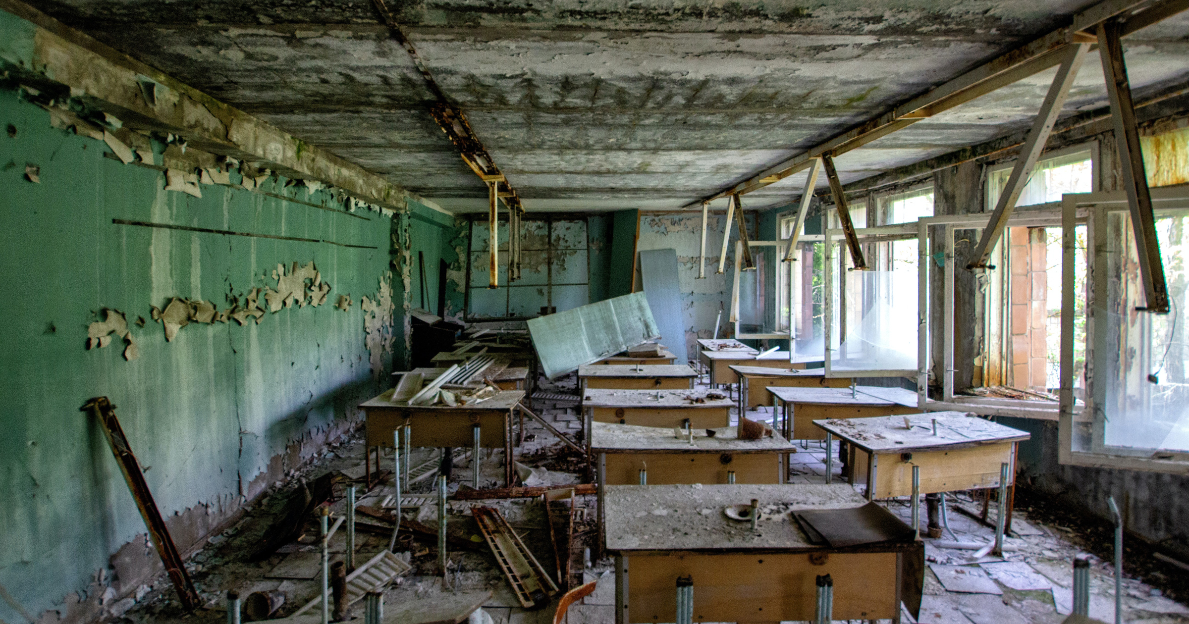 A photo of a wrecked classroom with paint peeling from the ceiling, desks turned over and broken.