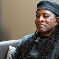 A man sitting with a black shirt and black cap on a couch