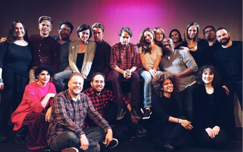 A group photo of the Experiments in Opera team against a dark pink background