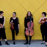 A string quartet standing in front of a yellow wall