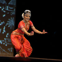 A dancer posing with arms extended to the audience in traditional attire