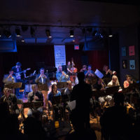 A large jazz ensemble performing in a crowded space.