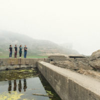 A group of people standing near a pond, with their reflection coming through