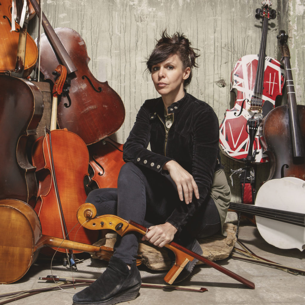 Helen Gillet surrounded by various cellos.