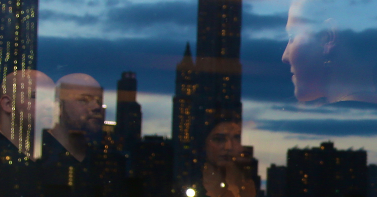 A photo of the staff members of Creatives Care shown reflected in the window of a high rise building foregrounding the Manhattan skyline.