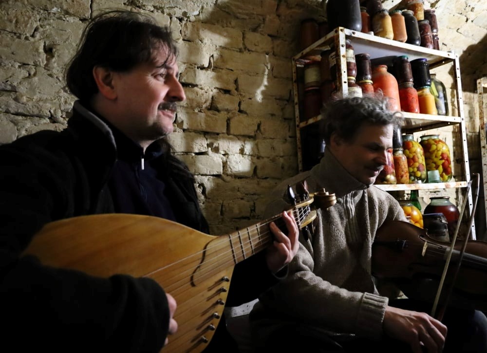 Two musicians performing on traditional Ukrainian instruments near shelves of preserves.