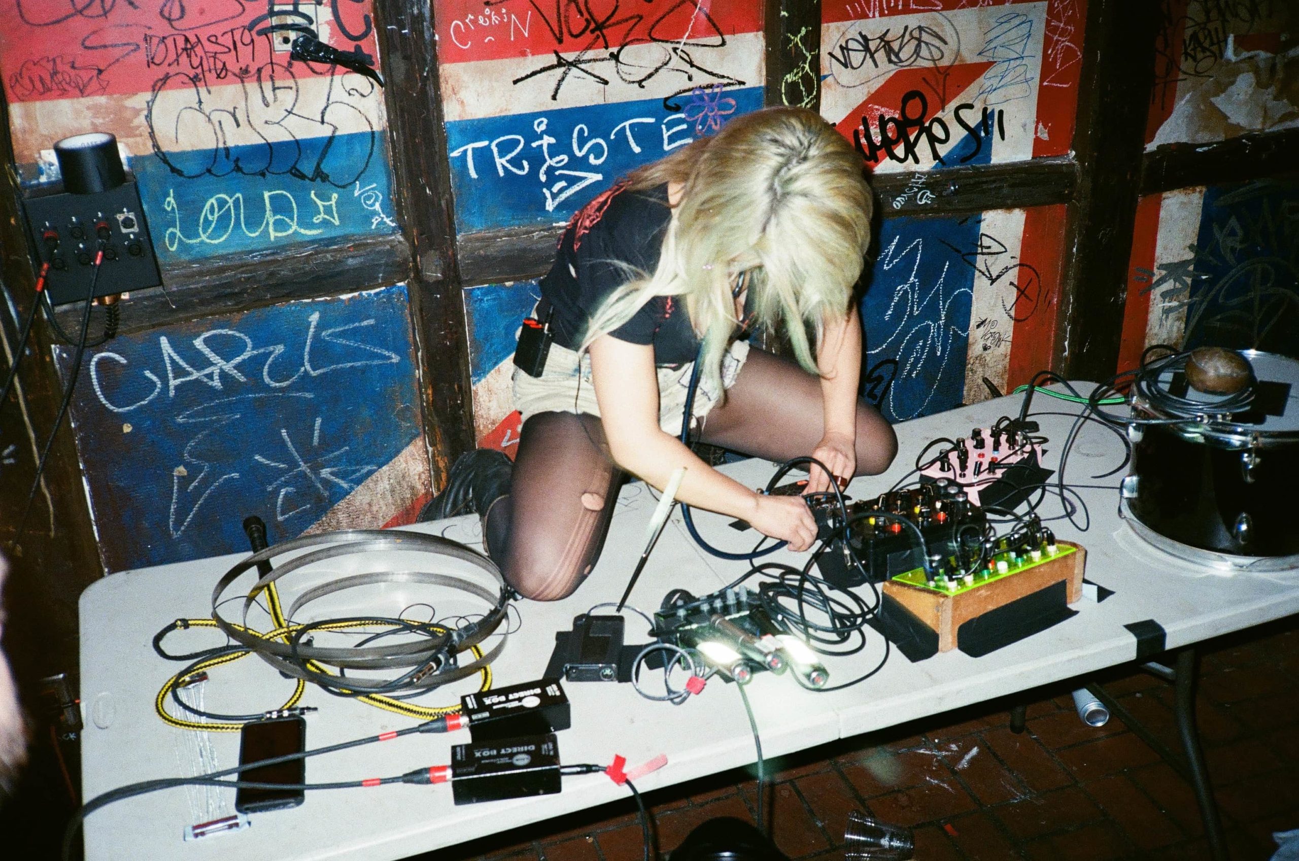 Victoria Shen in mid performance is crawling on a table filled with various electronic music producing gear.