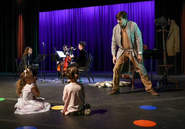 Children sit and musicians perform as John Liberatore narrates in a performance of his Owl in Five Stories 