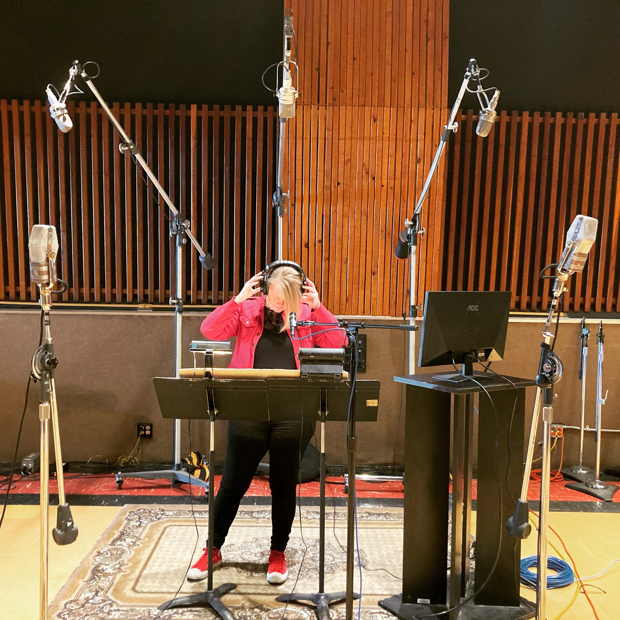 Catherine Joy surrounded by microphones listening to a track on headphones in a recording studio.