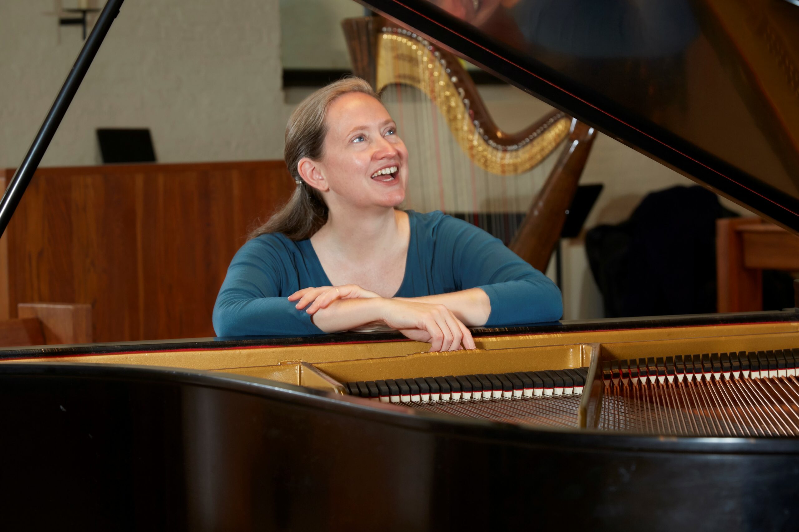 Rachel Grimes sitting in front of a grand piano with a harp in the background