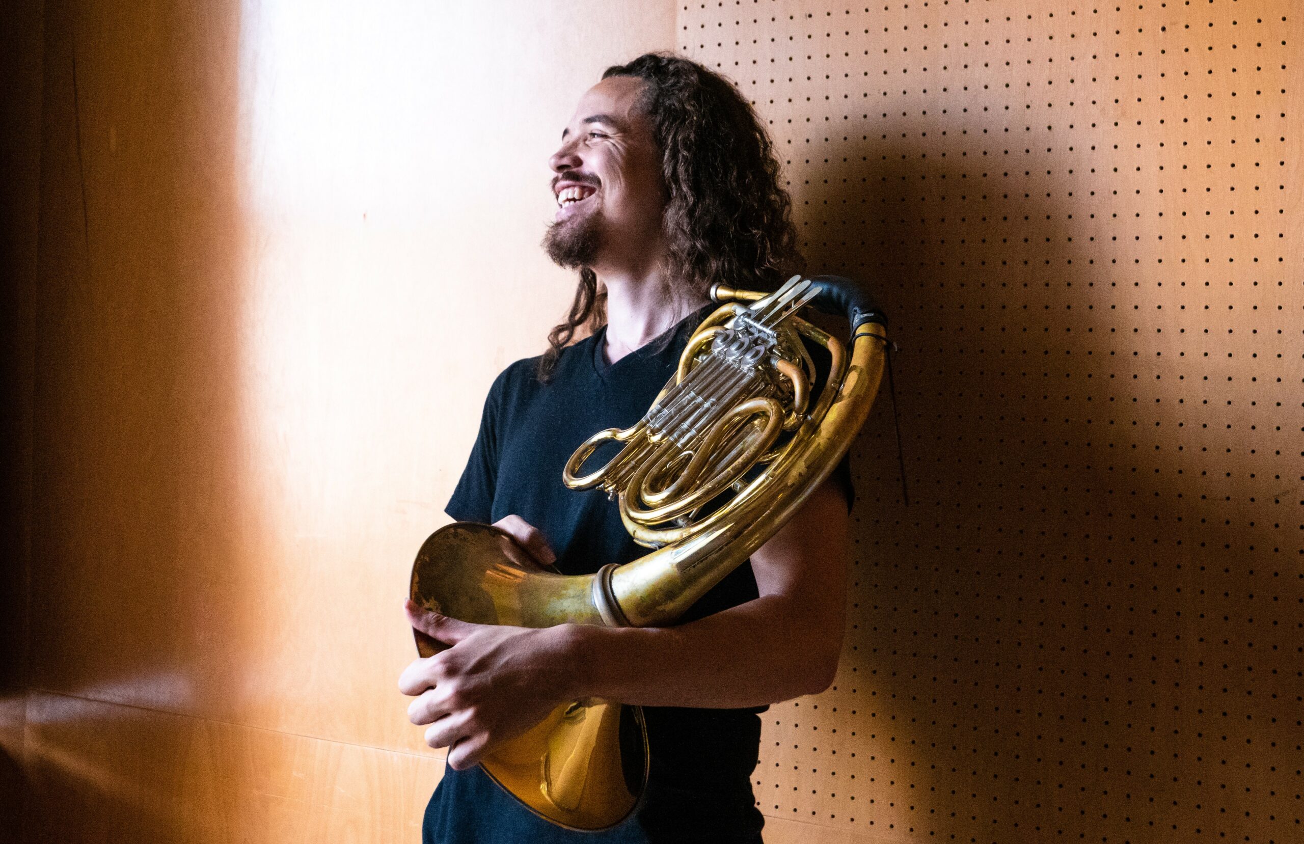 Tyler Taylor in an enclosed space holding a French horn