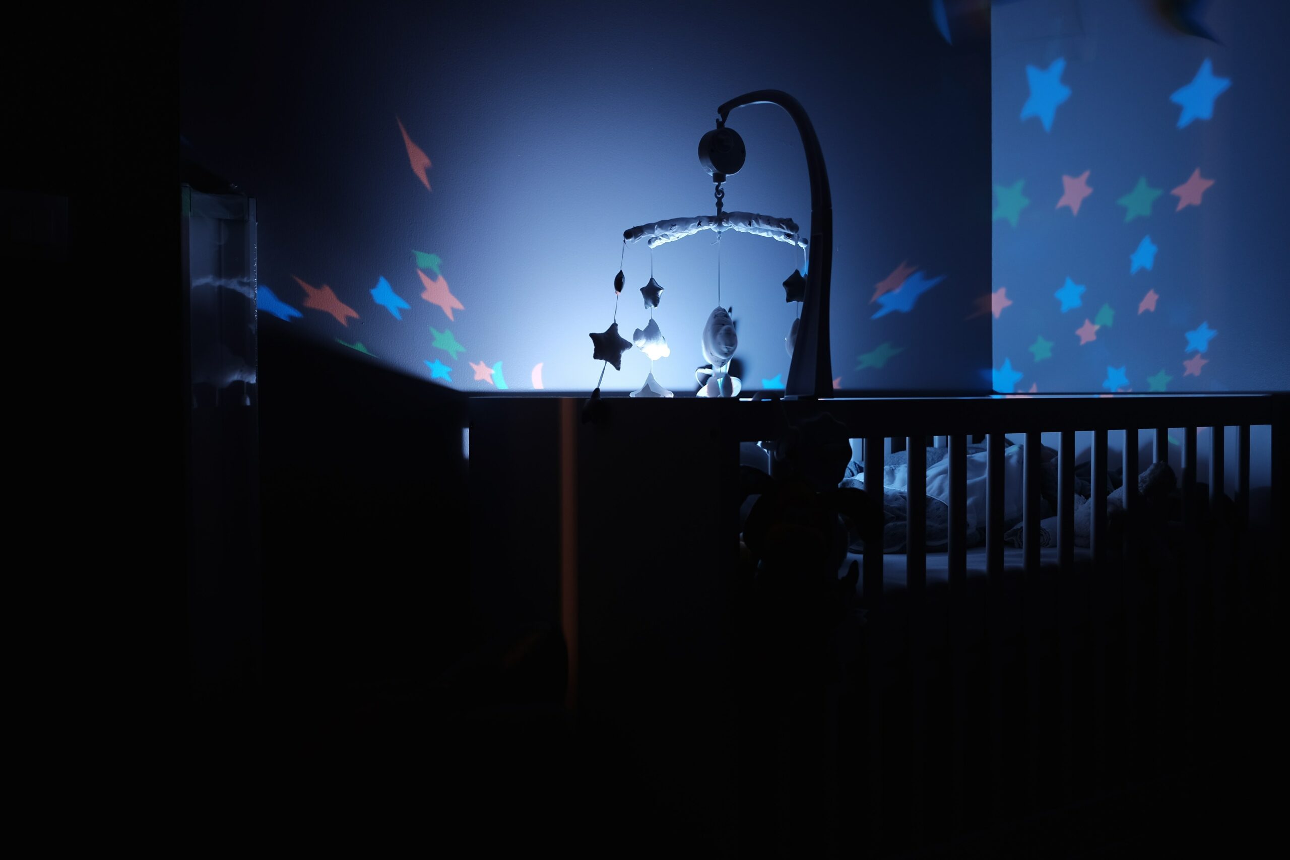 A night-time photo of a baby crib and dangling baby toys (photo by Bastien Jaillot from Unsplash)