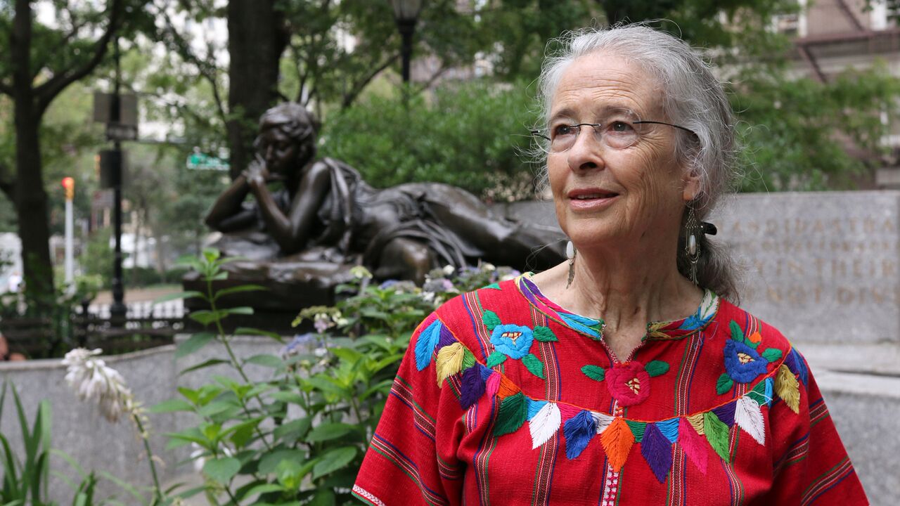 Eleanor Cory sitting in front of a sculpture and trees on a park bench